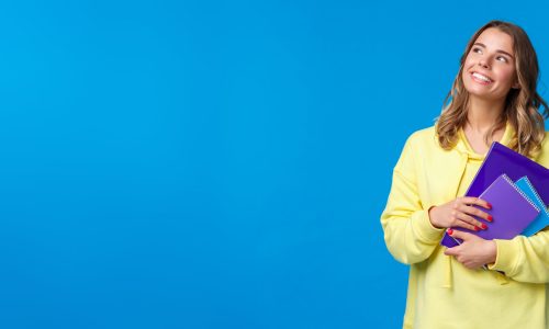 Back to school. Cute blond smiling european female student carry notebooks and learning material, look dreamy upper left corner smiling, thinking what she grab for lunch, blue background.